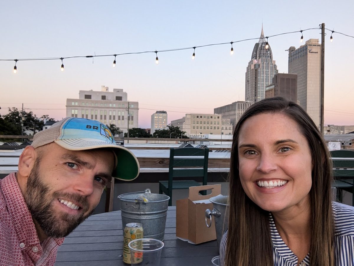 Brooks and Mandee at a rooftop table with the downtown Mobile skyline behind them at sunset