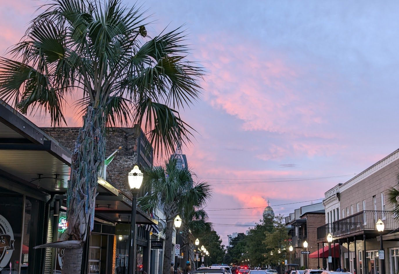 Dauphin Street in downtown Mobile at sunset, palm trees and string lights over the sidewalk